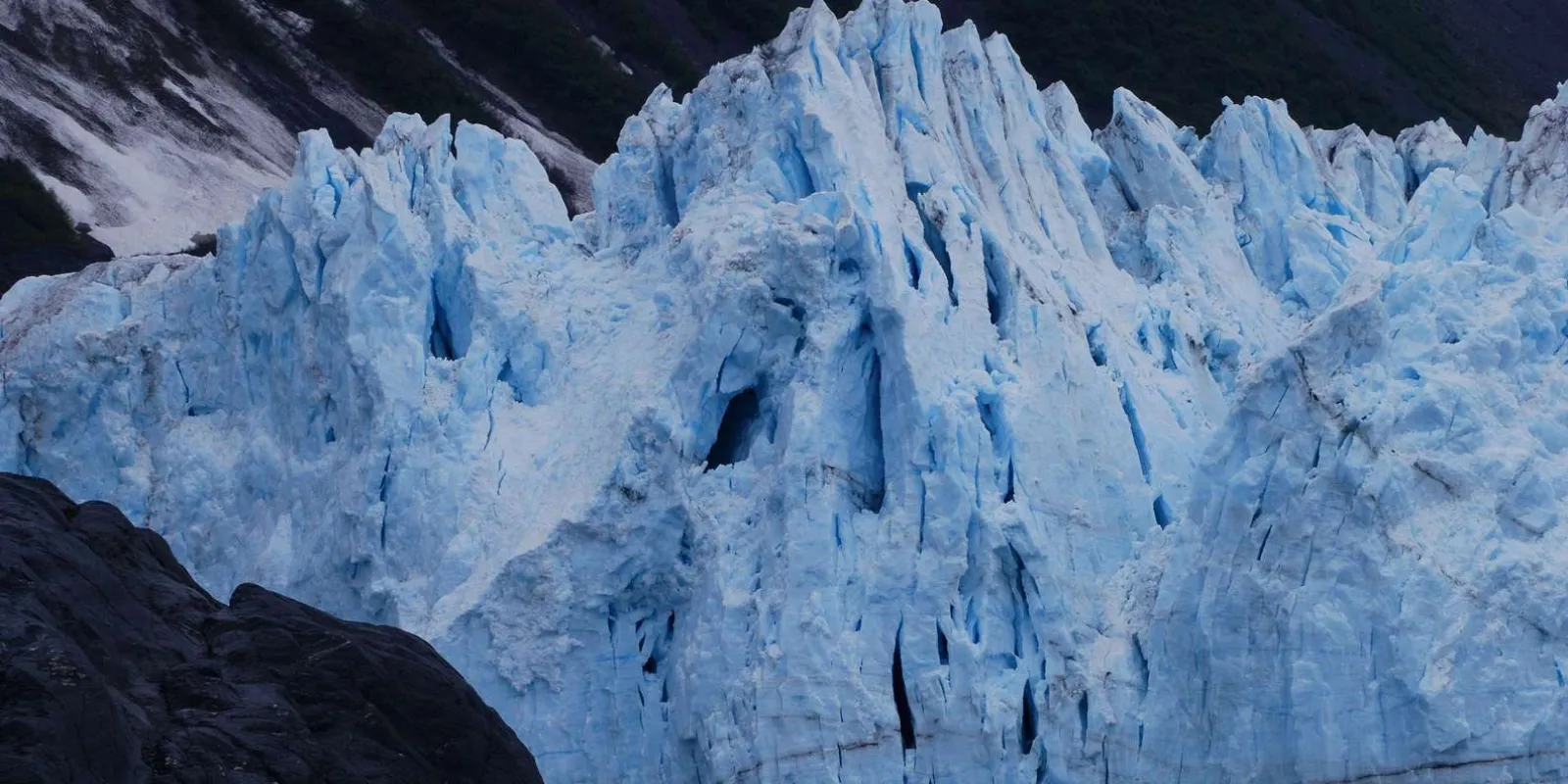 The heavily crevassed blue ice front of Blackstone Glacier, its pinnacles rising between dark rock walls