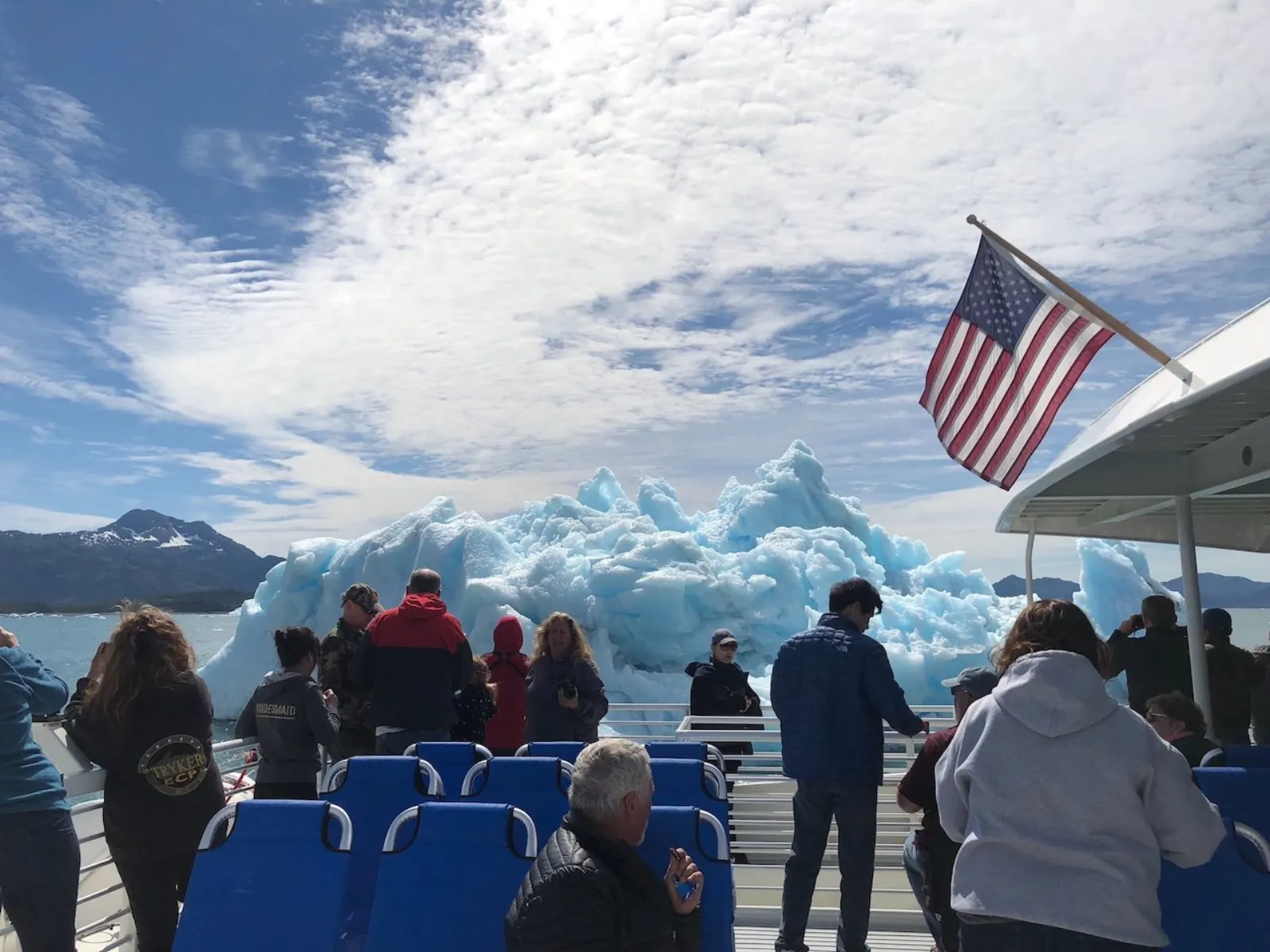 Passengers in winter coats lining the open deck rail beside the American flag as the boat passes floating icebergs