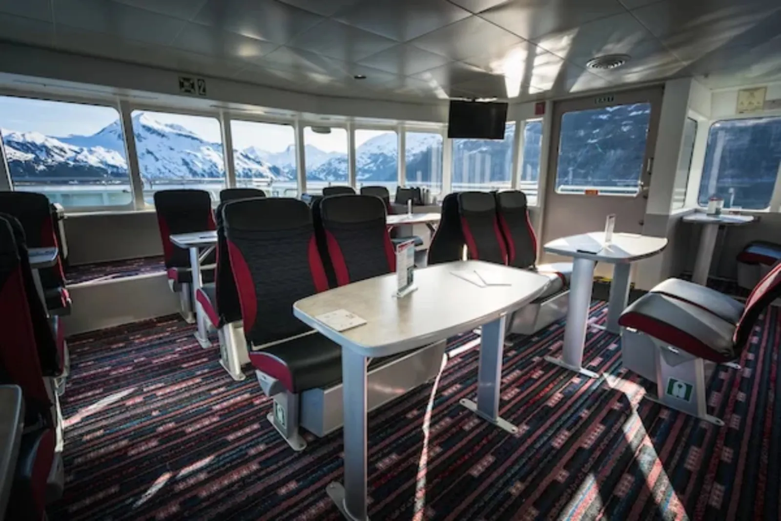 The heated indoor cabin of the catamaran, with tables, reclining seats and panoramic windows looking out to snow-covered peaks